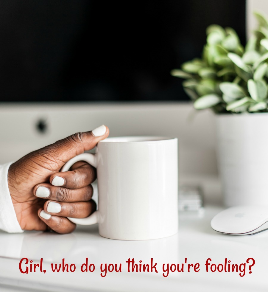 A black woman's hand holding a cup of coffee next to a plant in white planter.