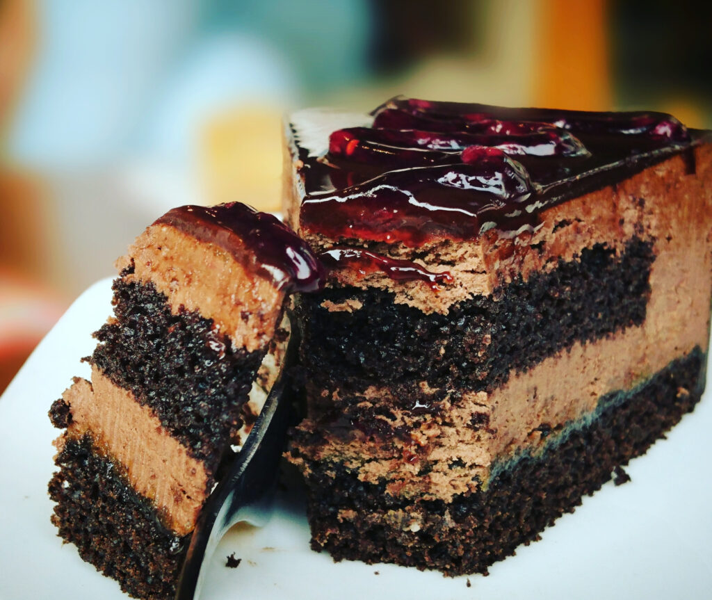 A slice of chocolate cake with chocolate mousse and raspberry ganache on top.